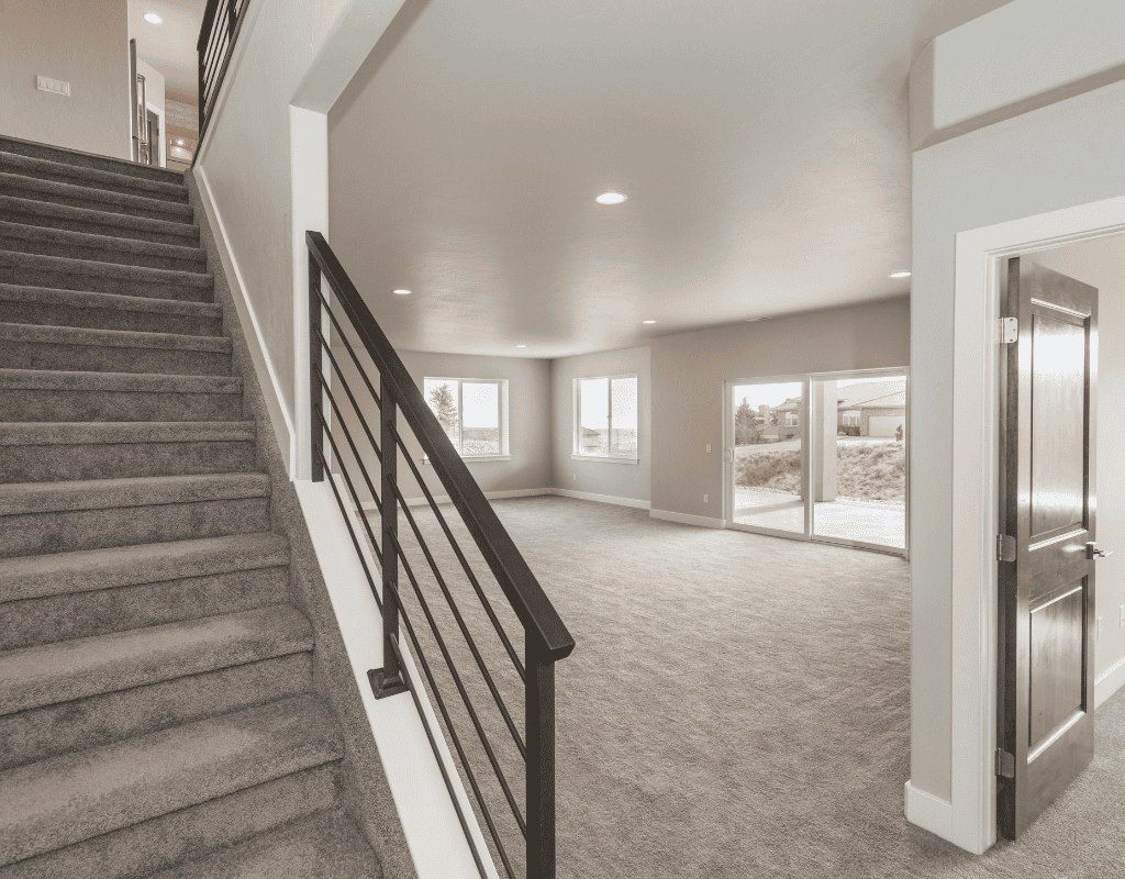 Open basement living area in Rexburg, ID with natural light, staircase railing, and completed drywall